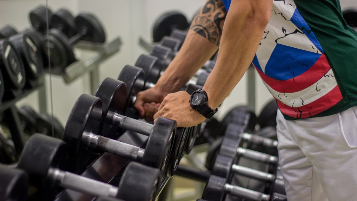 Man preparing to lift dumbbells in a gym, focusing on strength and fitness.